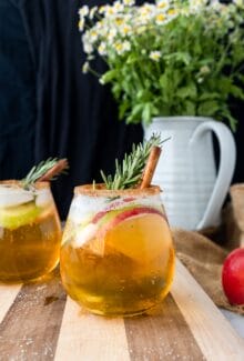 smoky apple cider sangria with cinamon, apple slices, and rosemary on a wood board