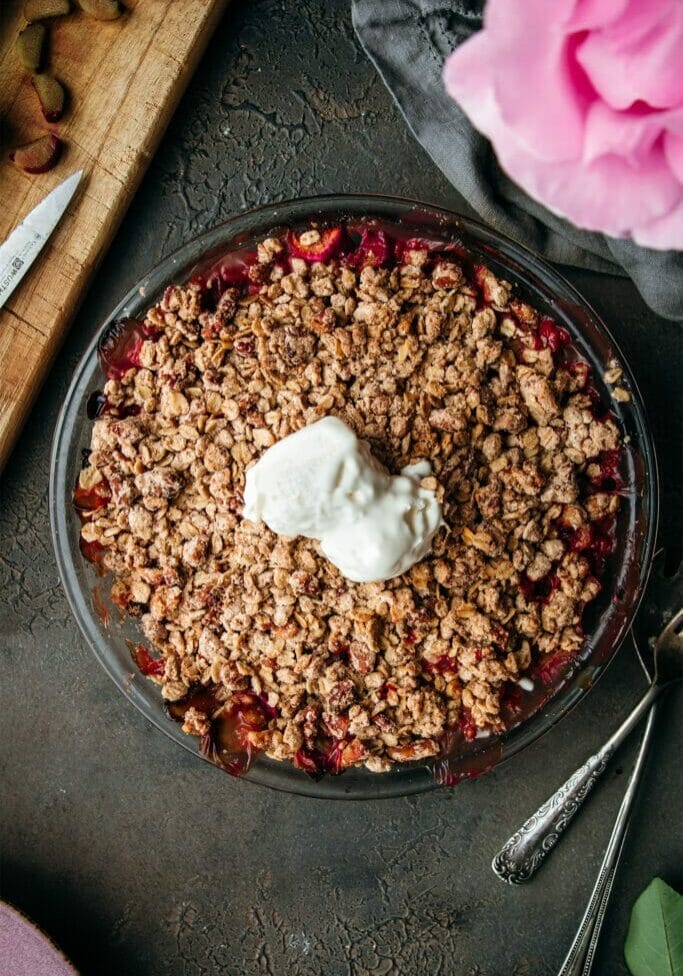 overhead shot of brown butter rhubarb crumble on a stone table with two scoops of vanilla ice cream