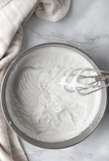 overhead shot of coconut whipped cream in a silver bowl next to a hand mixer