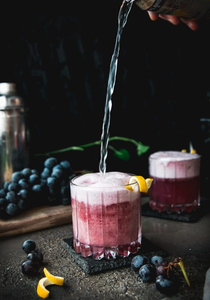 sparkling water pouring into a concord grape gin fizz cocktail