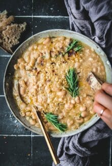 bowl of rosemary garlic braised white beans with a gold spoon and crusty bread