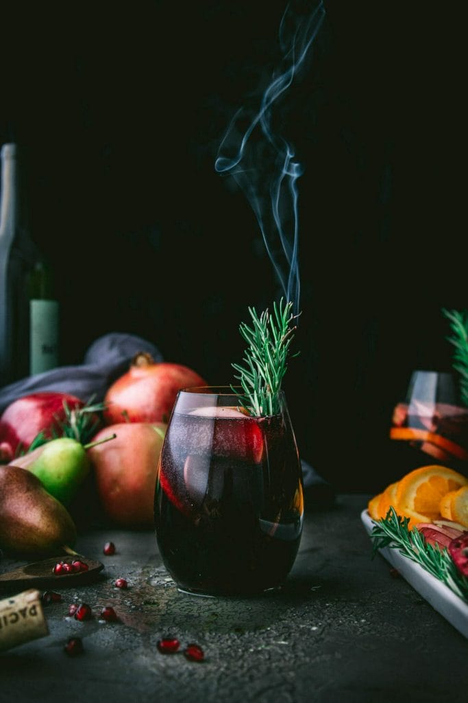 glass of autumn sangria with a burnt sprig of rosemary