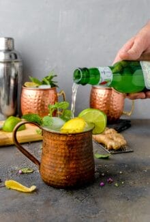 hand pouring ginger beer into copper moscow mule mug