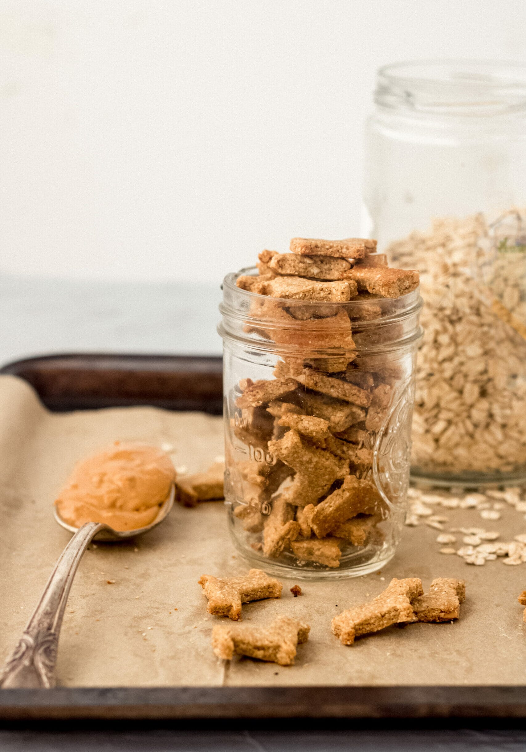 glass jar of homemade dog treats on a tray with a spoon of peanut butter