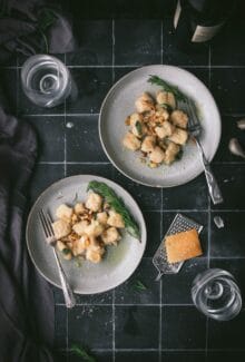two bowls of vegan leftover mashed potato gnocchi in an herb butter sauce on a black tile table