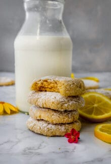stack of bright vegan lemon crinkle cookies with a bite taken out next to a glass of milk
