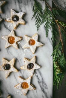 five vegan linzer cookies on a marble board next to a Christmas tree