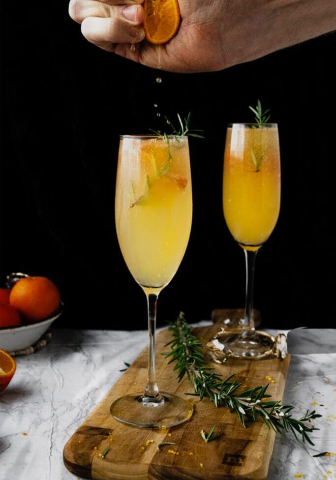 hand squeezing orange juice into a mimosa flute glass