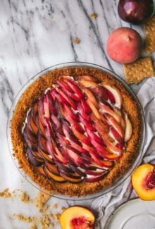 peaches and cream tart on a marble table next to sliced peaches and graham crackers