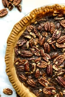 side birds eye view of vegan pecan pie in a pie plate on a white table