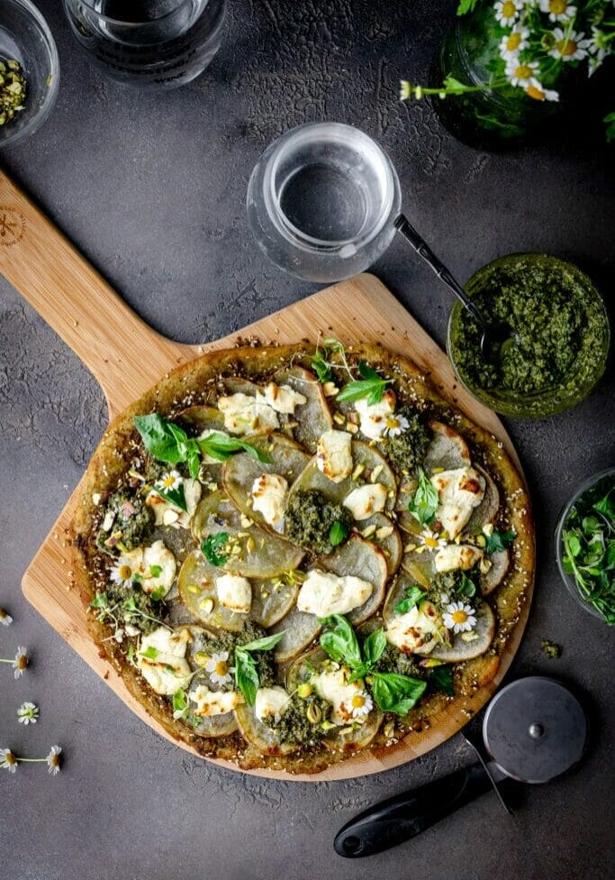overhead shot of pesto potato pizza on a pizza peel next to a glass of water