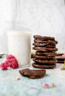 stack of vegan thin mint cookies next to a glass of milk and a pink flower