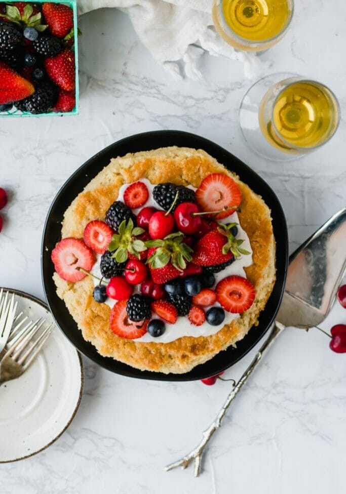 birds eye view of a vegan olive oil cake covered in berries on a black plate