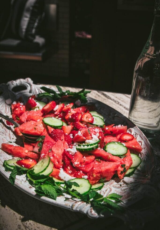 a high angle shot of watermelon, cucumber, and feta salad next to a bottle of water